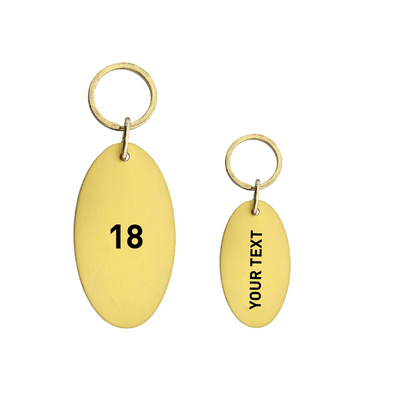 Two gold oval keychains with gold rings, one displaying the number '18' and the other with 'YOUR TEXT'.